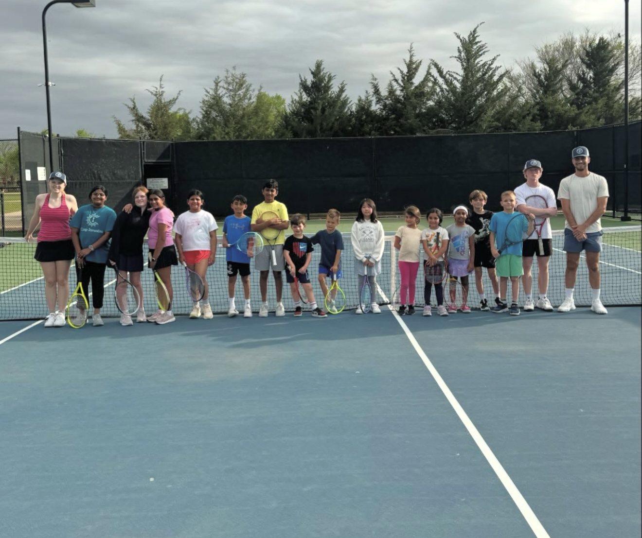 A Universal Rackets junior tennis clinic lined up at the net with their coaches
