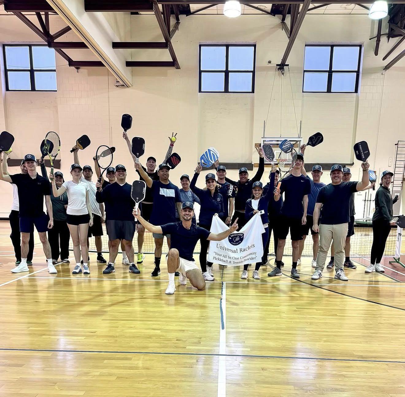 The Universal Rackets coaching team with paddles and racquets raised behind the company banner